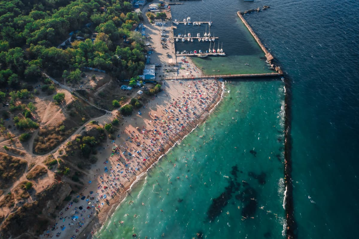Аэрофотоснимок пляжа: плотная застройка вдоль берега, прозрачная вода 