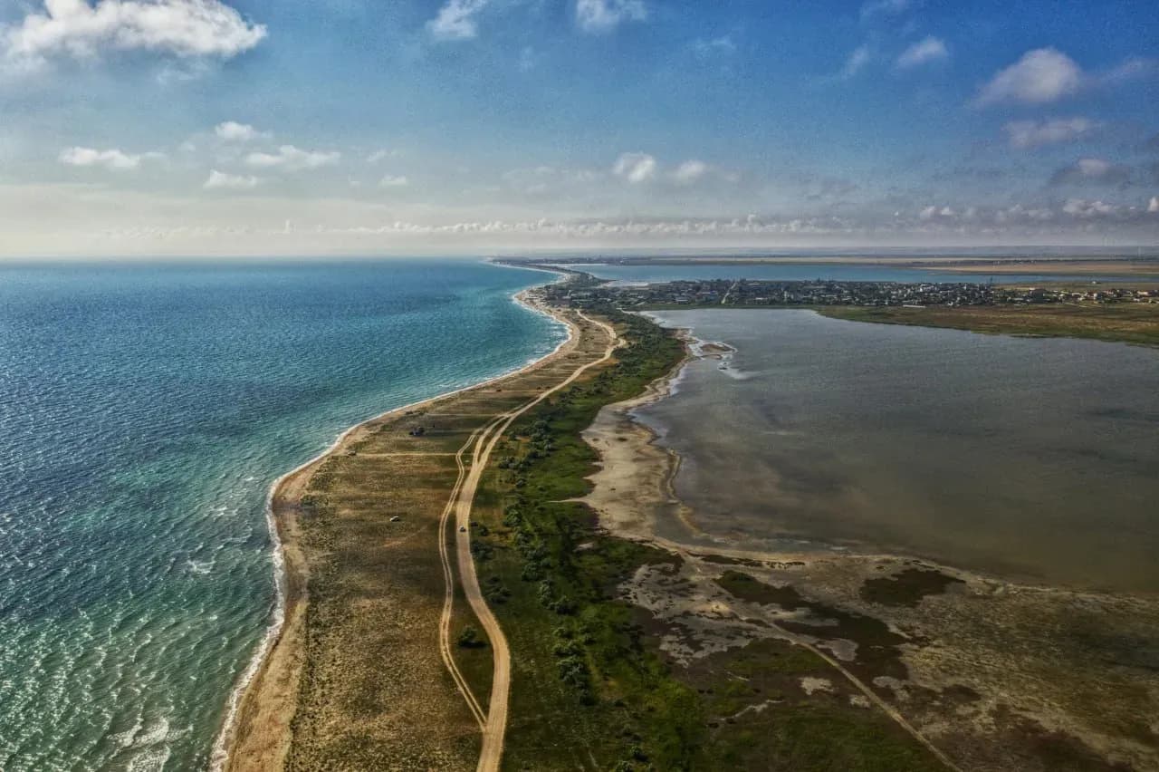 Длинная дорога вдоль Каспийского моря и лагун Мангистау с бирюзовой водой, солончаками и степным пейзажем.