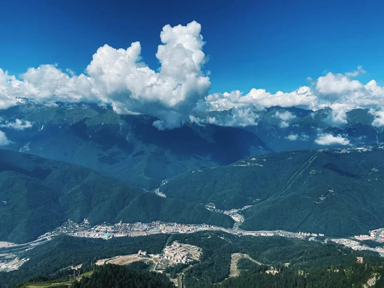 Панорама Красной Поляны с Кавказскими горами, облаками и курортной долиной.