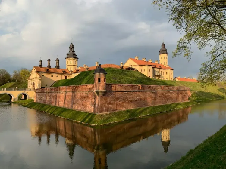   Замковый комплекс в Гродно с кирпичными стенами, водой и зелёной территорией.